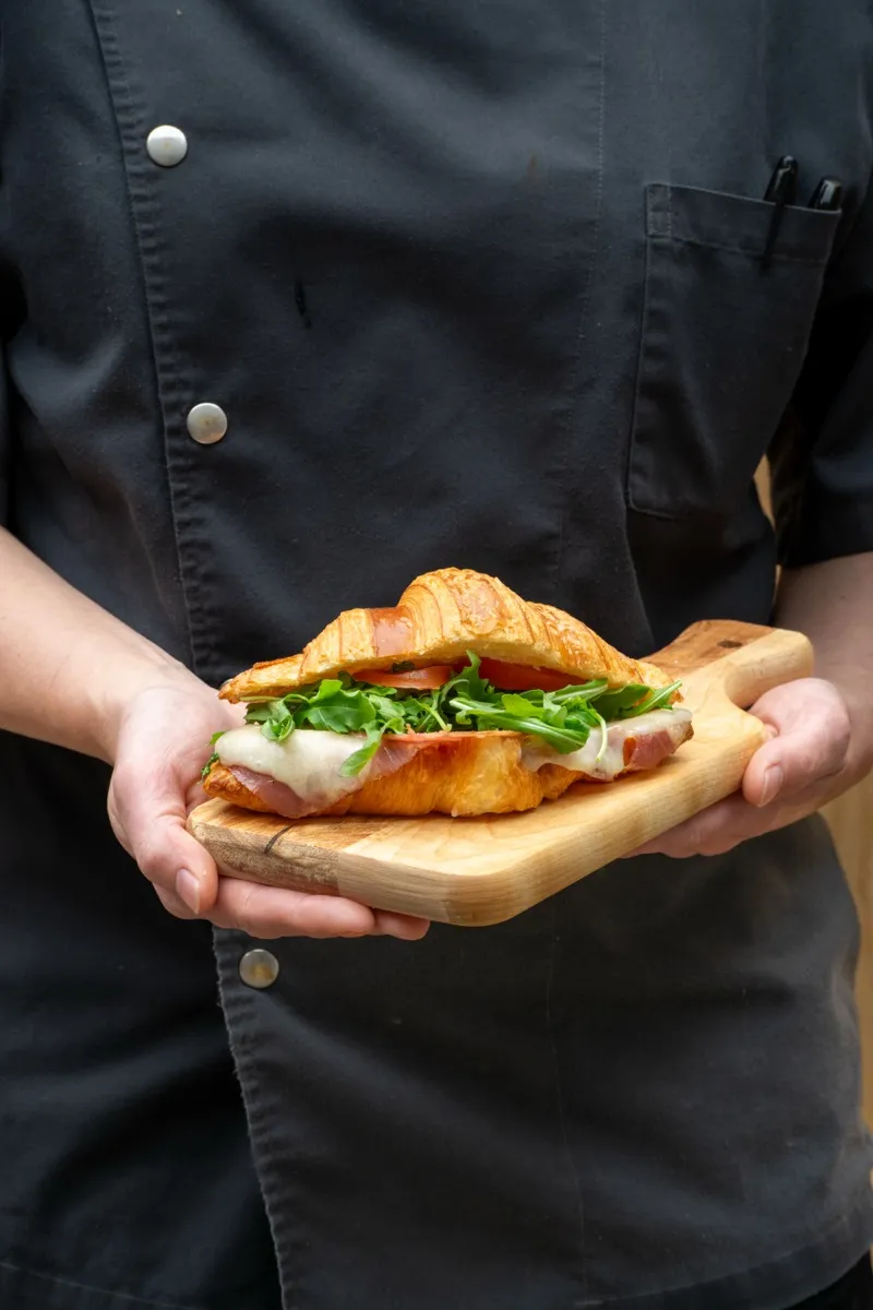 Fresh croissant sandwich on a wooden board held by a chef